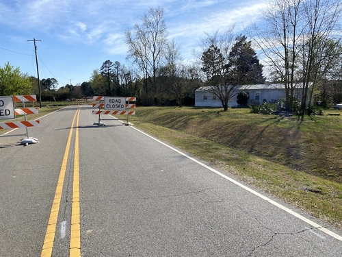 DOT allegedly failed to set targets to reduce driving, required as part of settlement over Wake County toll road A photo of Rhodes Road and signs that say "Road Closed" with a mobile home in the background. The Blue Skies Mobile Home Park has been cut off to the south by the Complete 540 toll road.