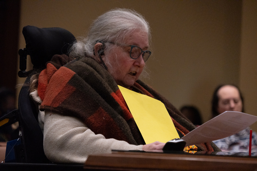 Nebraska lawmakers propose disability, racial impact statements for certain legislation Kathy Hoell wears a flannel blanket around her shoulders reading her prepared testimony before the Legislature's Executive Board. In her hands she holds a yellow folder that contains her testimony.
