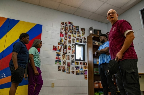 First floods, now fires: How neglect and fraud hobbled Prichard Two men, one in a blue shirt and one in a maroon one, stand in front of a wall with photos on them. Two children stand to the left of the wall.